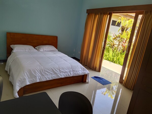 Un dormitorio con cama de madera, ropa de cama blanca, un escritorio pequeño y vista a zonas verdes a través de una puerta corredera.
