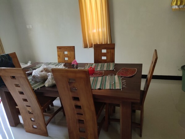 A dining area with a wooden table and chairs, a plastic bag on the table, and a glass on the table. - Martin's Guest House (Gianyar)
