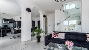 Un espace de vie moderne avec un canapé noir, une table basse en verre et un coin repas avec une table dressée pour deux personnes.
