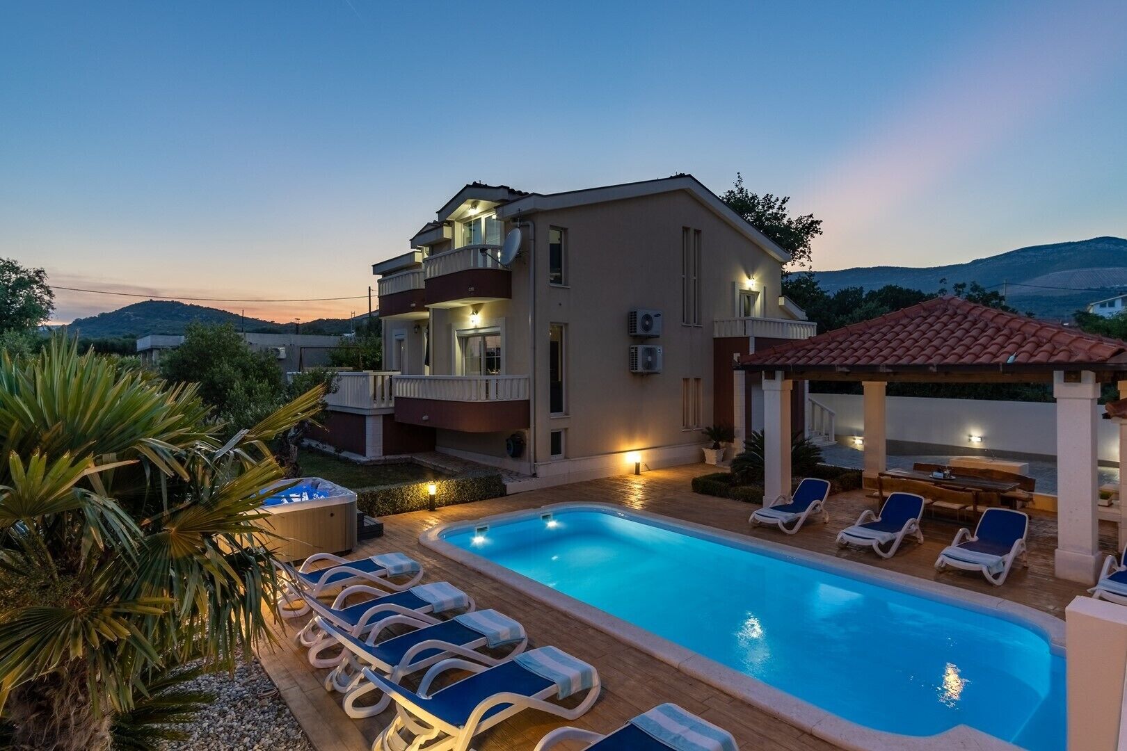 A two-story house with a swimming pool, outdoor seating, and a view of the hills.