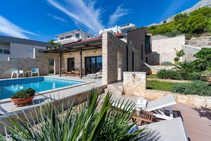 A modern villa with a swimming pool, outdoor seating, and a stone facade. - Villa Oslo - luxury place with sea views & heated pool, 300m from sandy beach (Omis)