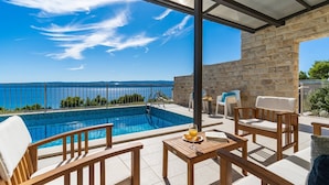 Ein Poolbereich mit Steinmauer, Sitzgelegenheiten im Freien und Blick aufs Meer.