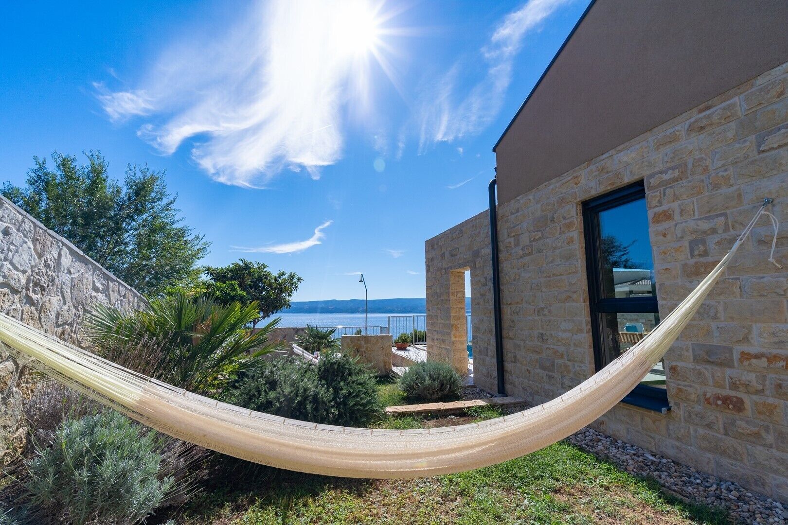 Un hamac dans un coin du jardin, près d’un bâtiment en pierre, avec vue sur la mer.