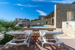 A poolside area with lounge chairs, a table, and a stone wall. - Villa Oslo - luxury place with sea views & heated pool, 300m from sandy beach (Omis)