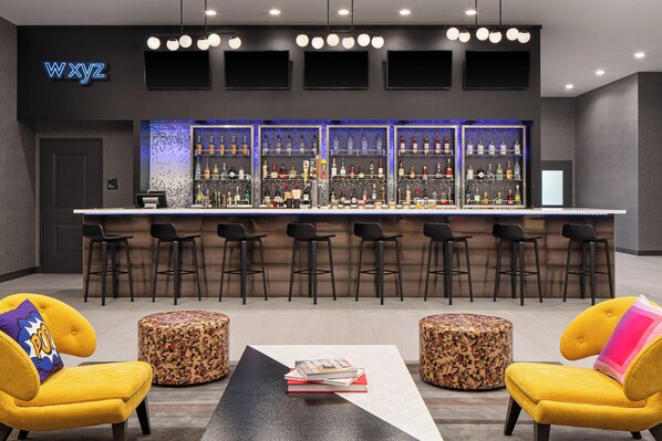 Un espace bar proposant différents types de sièges, un panneau lumineux au néon et une variété de bouteilles d’alcool.