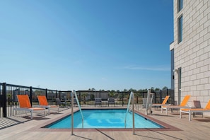 A rectangular pool with a metal ladder, surrounded by lounge chairs with orange cushions.