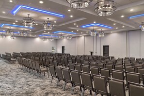 Une salle de conférence avec des rangées de chaises, des lustres et un sol recouvert de moquette.