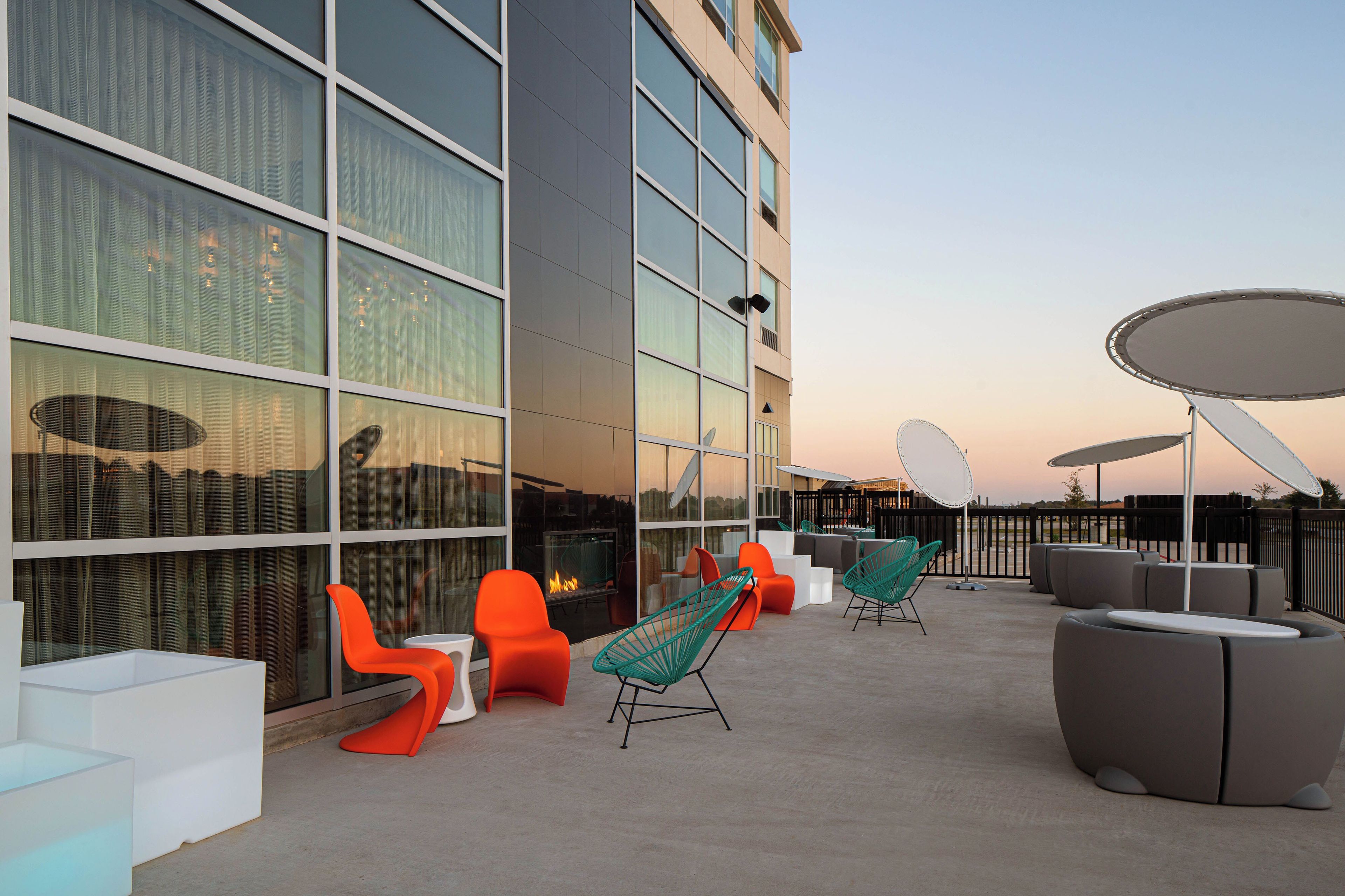 An outdoor seating area with modern furniture, a fire feature, and a view of the building's exterior.