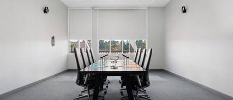 A conference room with a long table, chairs, a projector, and a window with a view of trees.