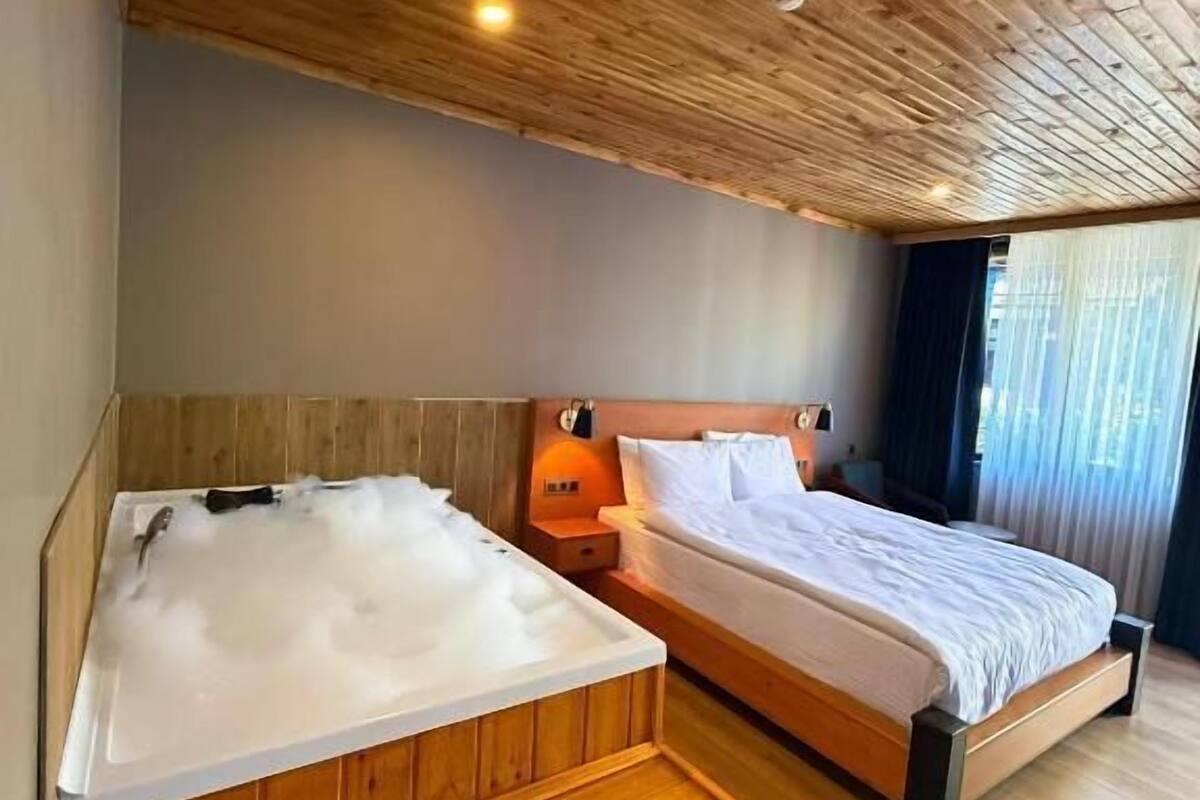 A room with a wooden ceiling, a bed, a wooden bench, and a hot tub.
