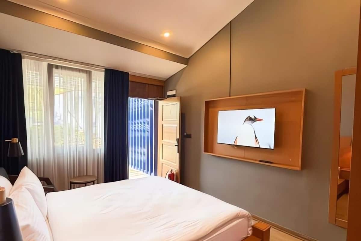 Ein Hotelzimmer mit einem Bett, einem an der Wand befestigten Fernseher und einem Fenster mit Vorhängen.
