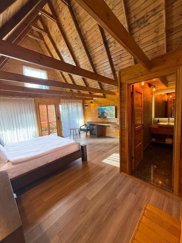 Une pièce spacieuse avec un plafond en bois, un lit, un bureau et une salle de bain.