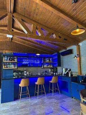Una zona de bar con vigas de madera, una barra azul y tres taburetes de bar.