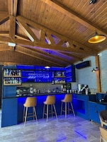 Una zona de bar con vigas de madera, una barra azul y tres taburetes de bar.