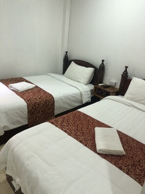A hotel room with two single beds, each with a white bedspread and a red patterned runner. There is a wooden nightstand with a lamp and a telephone. - Little Freedom Friendlys Place (Luang Prabang)