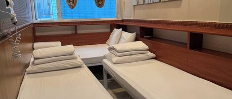 A hotel room with two single beds, a wooden bench, a small table, a hairdryer, and a window with curtains.