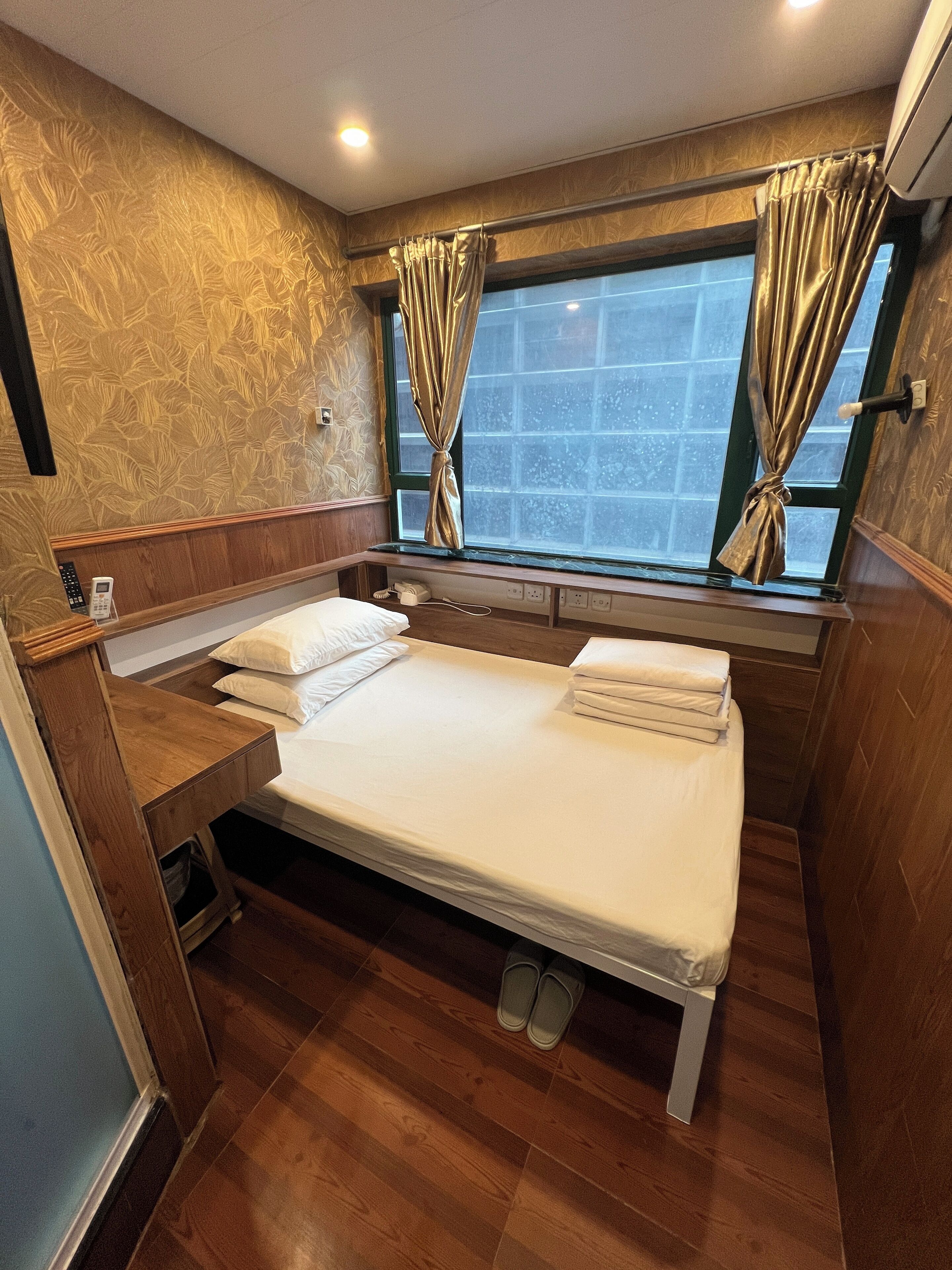 A compact bedroom with a single bed, wooden flooring, a window with curtains, and a built-in bench.