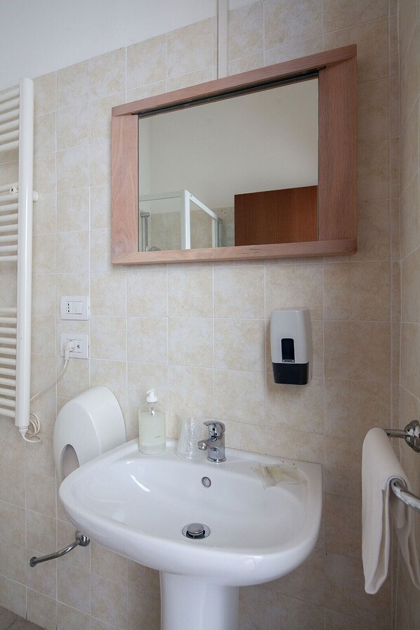 Un baño con lavamanos blanco, un espejo, dispensador de jabón y perchero para toallas.