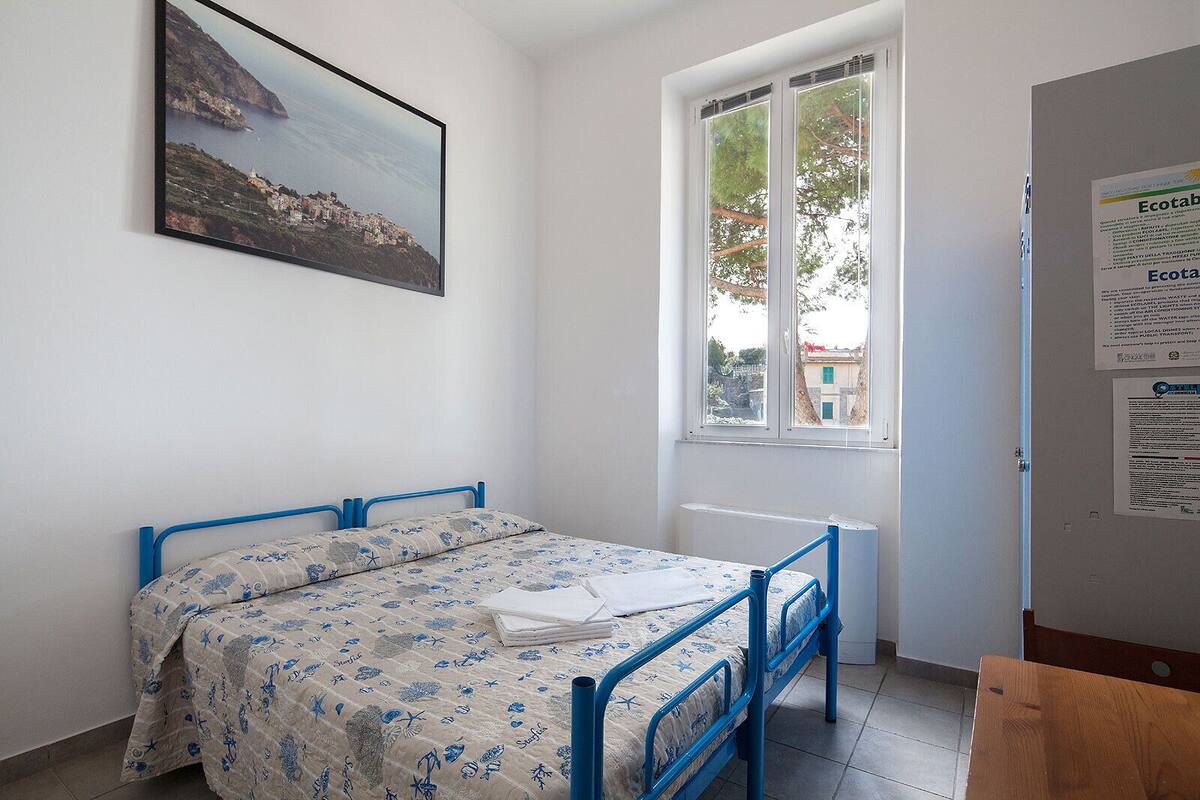 A bedroom with a bed, a window, a radiator, and a poster on the wall.