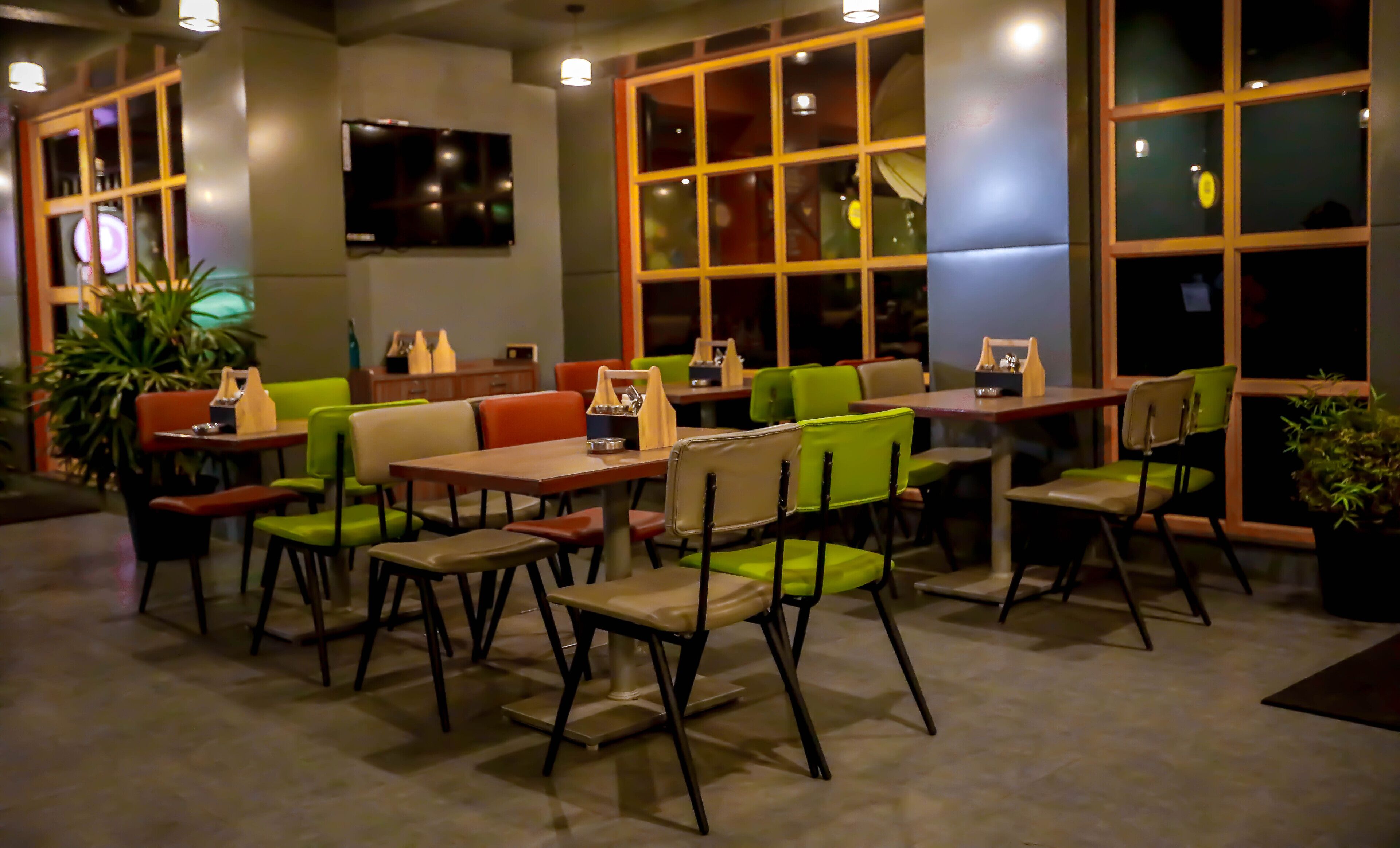 Un restaurante con cabinas y mesas, algunas con sillas verdes, y un televisor montado en la pared.