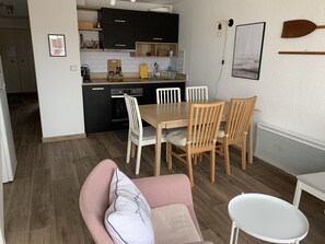 Una cocina moderna con armarios negros, una mesa de comedor de madera y sillas blancas. Hay un cuadro en la pared y una pequeña mesa blanca en primer plano.