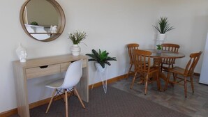 A room with a wooden desk, a white chair, a round table with wooden chairs, and potted plants. - Adventures at Sue's Retreat ....... (Mount Gambier)