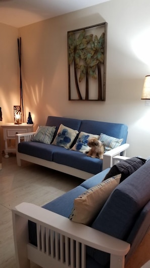 Een woonkamer met een blauwe bank, een kleine hond en een schilderij aan de muur.