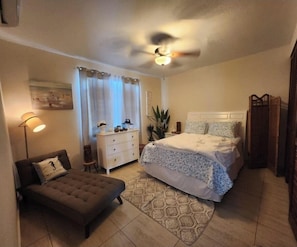 Un dormitorio con cama, mesita de noche, lámpara, silla y ventilador de techo.