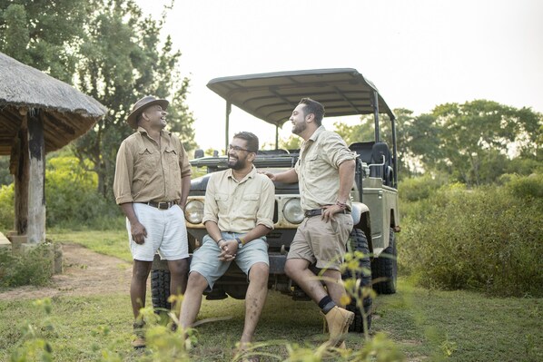 Three people sitting on a vehicle with a thatched roof structure in the background. - Ceylon Wild Safaris Yala (Thissamaharama)