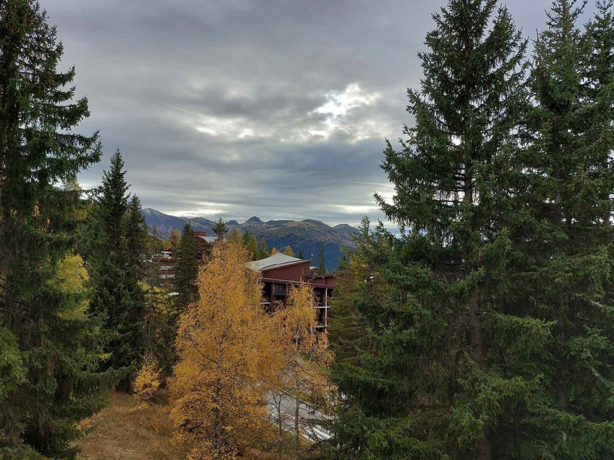 A lodge with a mountain view, surrounded by evergreen trees and a few autumn-colored trees.