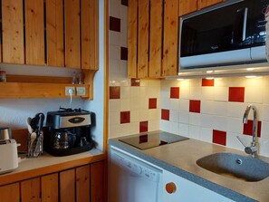 A compact kitchen with wooden cabinets, a microwave, a coffee maker, and a dishwasher.