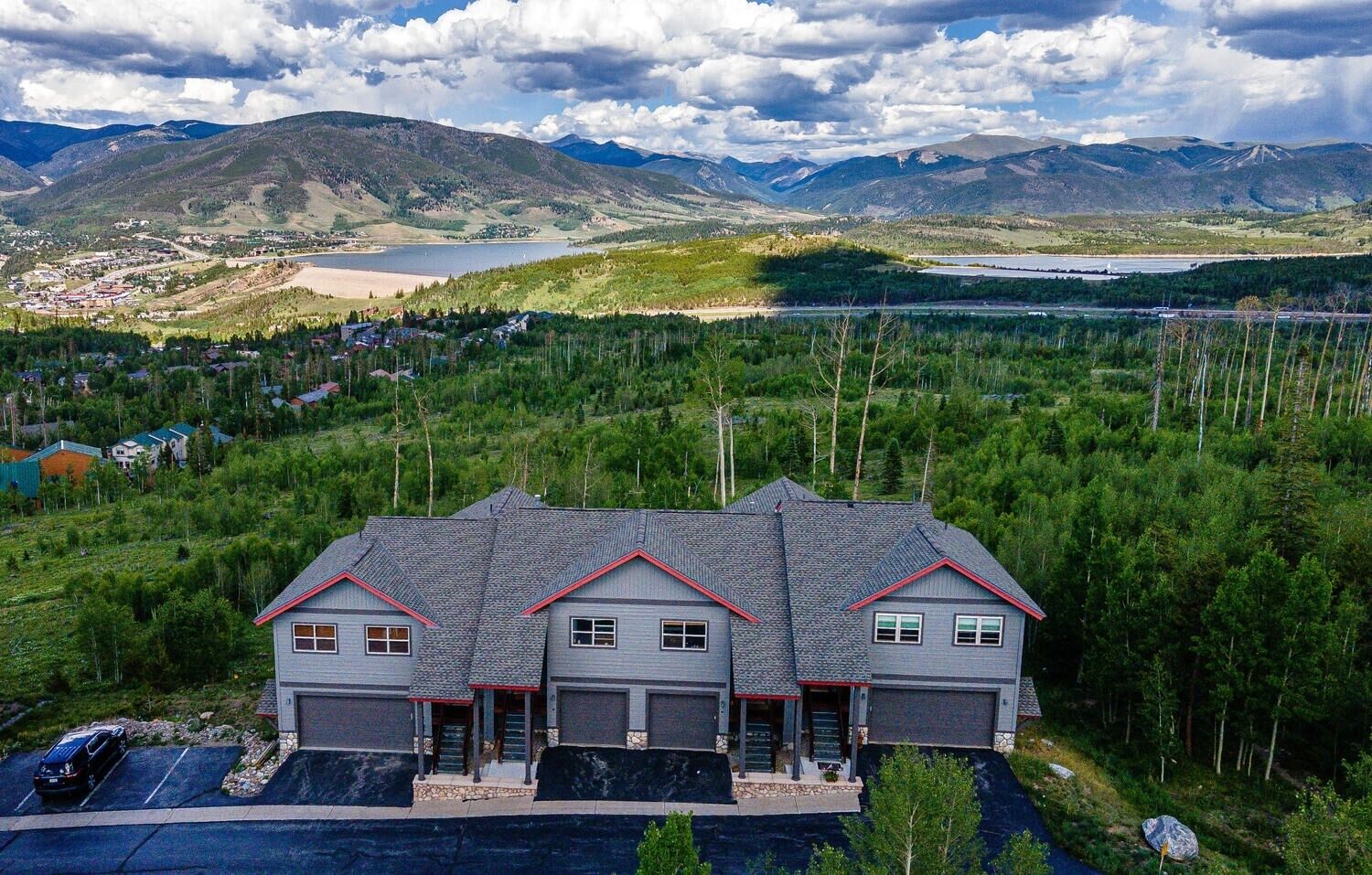 A large, modern house with a garage, surrounded by lush greenery and mountains in the background.