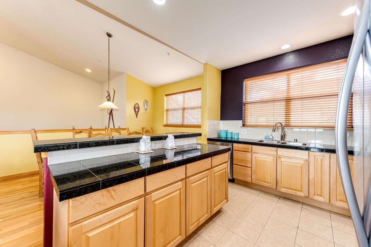 A modern kitchen with wooden cabinets, a black granite countertop, and a stainless steel refrigerator.
