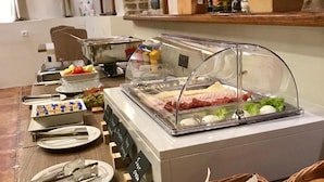 A buffet setup with various food items, including a glass display case with meat, a bowl of croissants, and a tray of bread. - M House Belgrade (Belgrade)