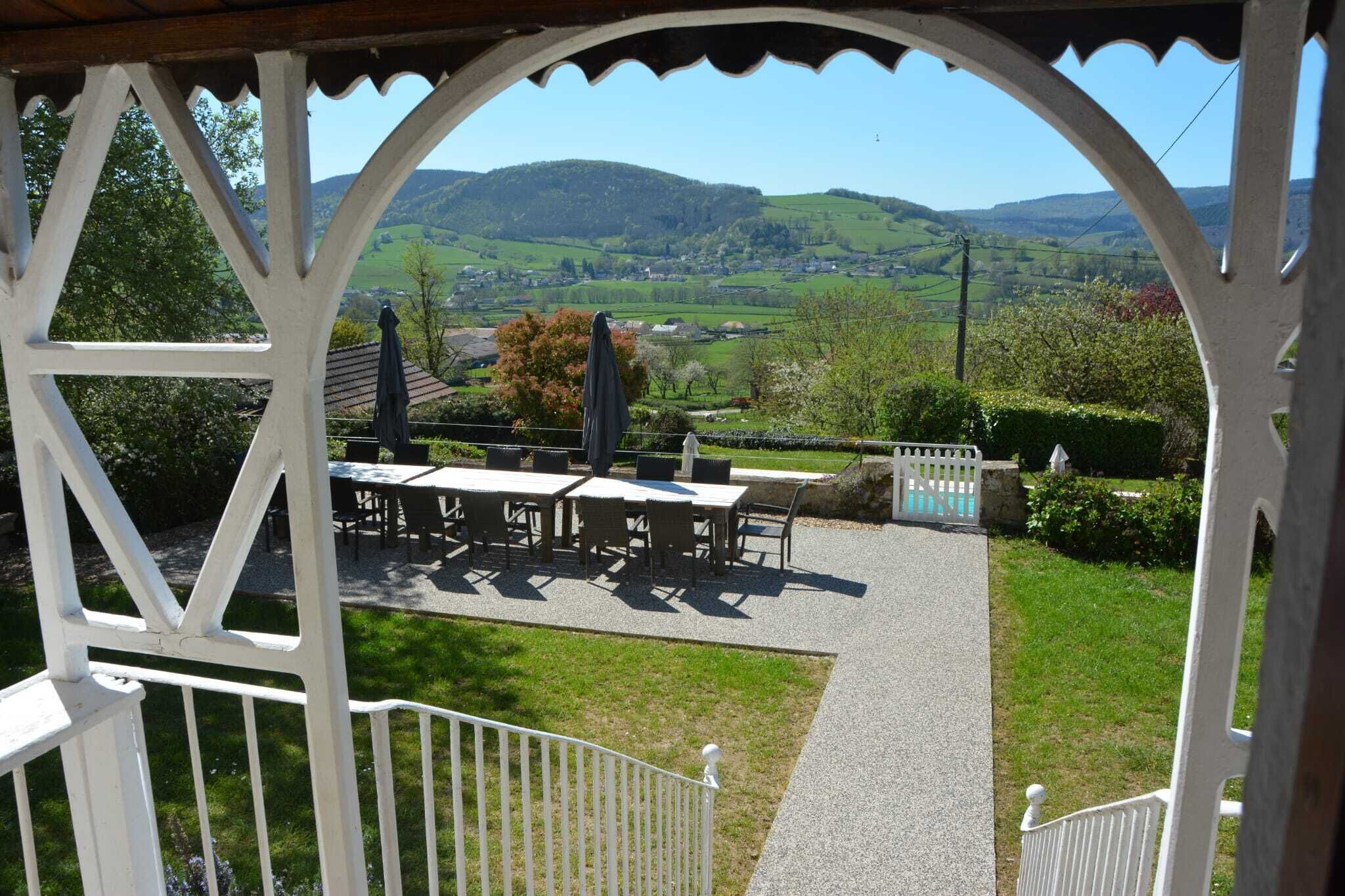 Ein überdachter Außenbereich mit Tischen und Stühlen, Blick auf ein grünes Tal und ein weißer Zaun.