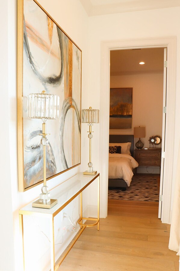 Hotelkamer met een groot abstract schilderij, twee bedlampen, een bed met een rug met patroon, en een nachtkastje met spiegel en decoratieve objecten.