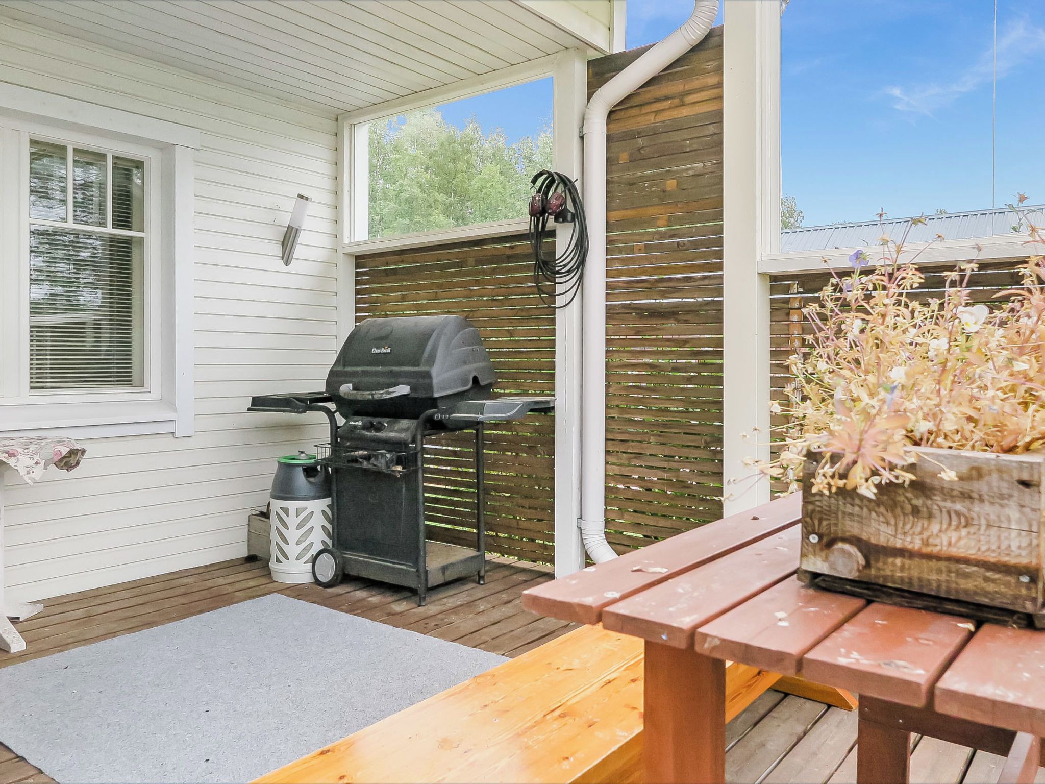 Un espace extérieur abrité comprenant un barbecue, une poubelle et un banc en bois.