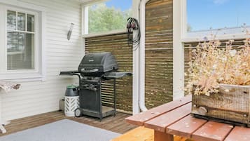 Un espace extérieur abrité comprenant un barbecue, une poubelle et un banc en bois.