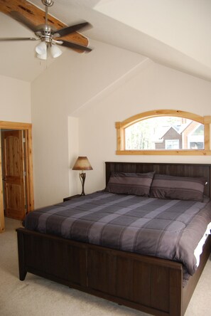 Une chambre avec un lit en bois, un ventilateur de plafond, une fenêtre donnant sur un beau paysage et une lampe.