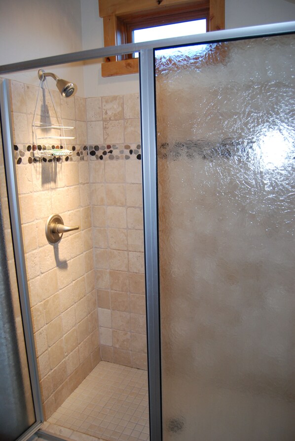 Eine begehbare, gläserne Dusche mit Handbrause und am Wand montiertem Wasserhahn.