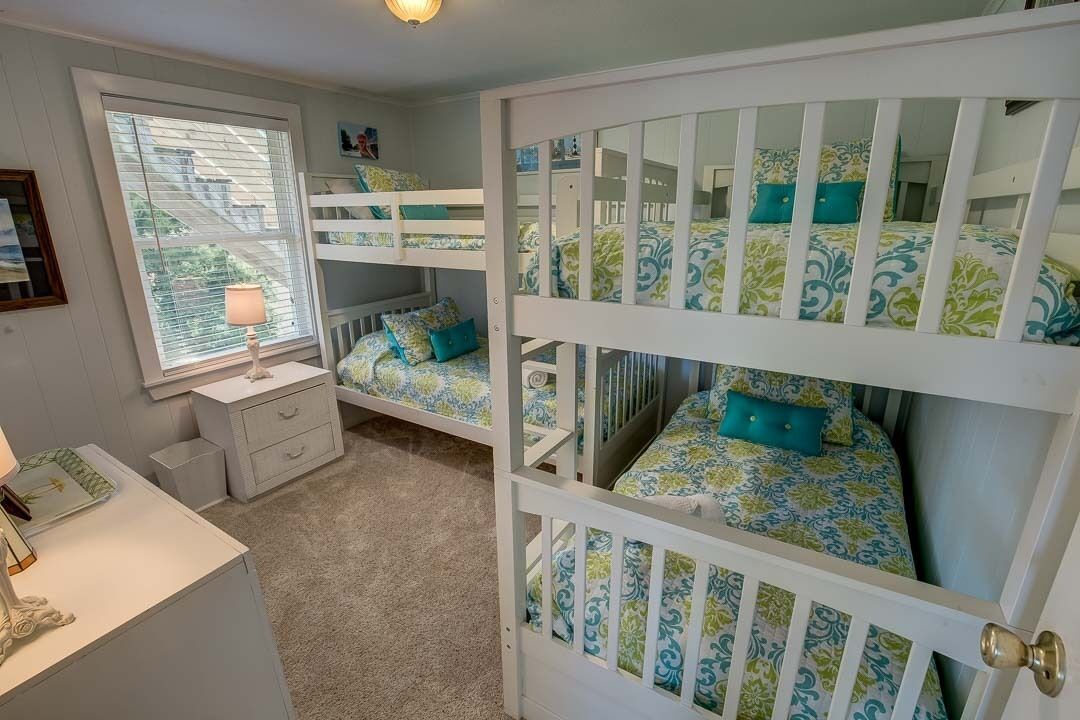 Una habitación con literas, una mesita de noche con lámpara y una ventana con persianas.