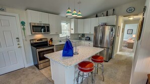 Una cocina moderna con armarios blancos, electrodomésticos de acero inoxidable, una isla central con taburetes e iluminación colgante.