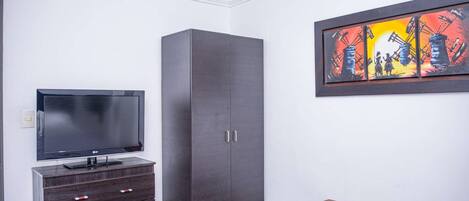 A bedroom with a bed, a TV on a dresser, a wardrobe, and a painting on the wall.