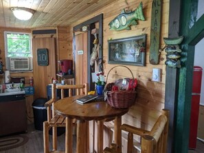 Ein Holzinterieur mit einem Esstisch, Stühlen, einem Korb und Wanddekorationen, darunter Fische und ein Schild.