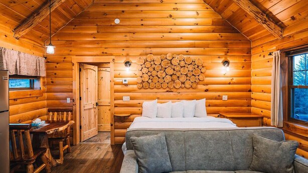 L’intérieur d’une cabane en rondins comprend un lit, un canapé, une table à manger et un mur fait de rondins empilés.