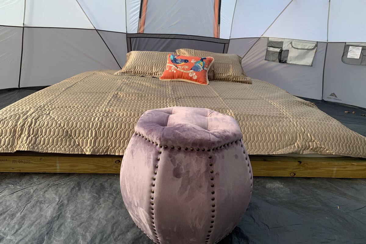A tent with a bed, pillows, and a cushion.