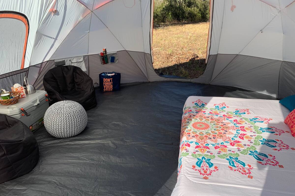 A tent interior with a bed, a storage box, a bean bag, and a bag with a motivational message.