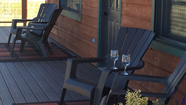 Une terrasse en bois avec deux fauteuils Adirondack et une table sur laquelle sont posés deux verres à vin.