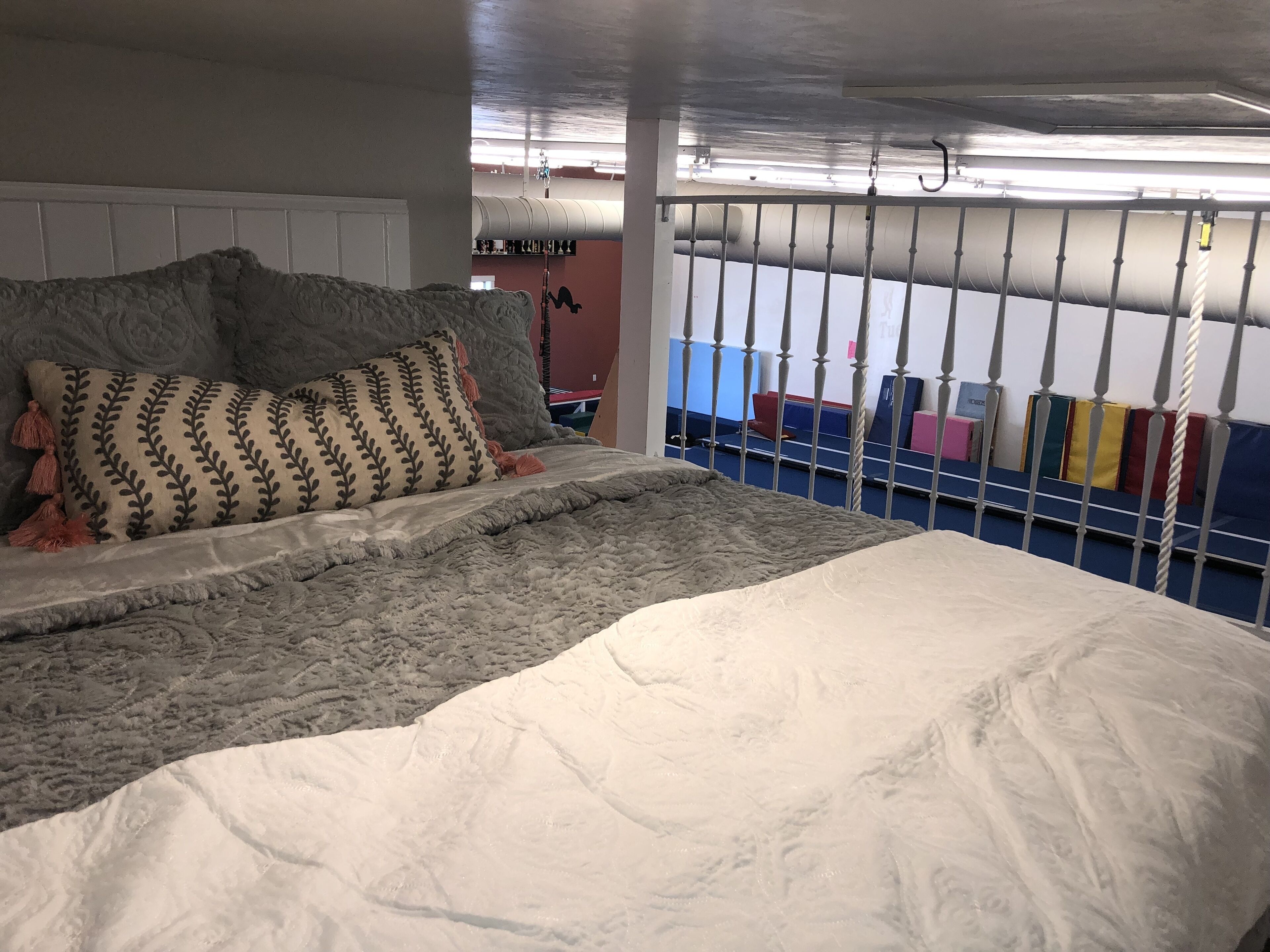 Un dormitorio con cama, almohadas, una colcha, una ventana con persianas y vistas a un gimnasio.