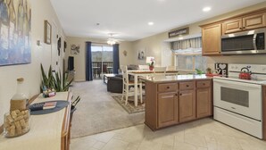 A modern kitchen with wooden cabinets, a built-in microwave, and an oven. There is a dining area with a table and chairs, and a view of the outdoors through a large window. - 3 Min to SDC. Walkin 2BR,2 Bath. condo, beautiful view of TRL and the Ozark Mtns (Branson)
